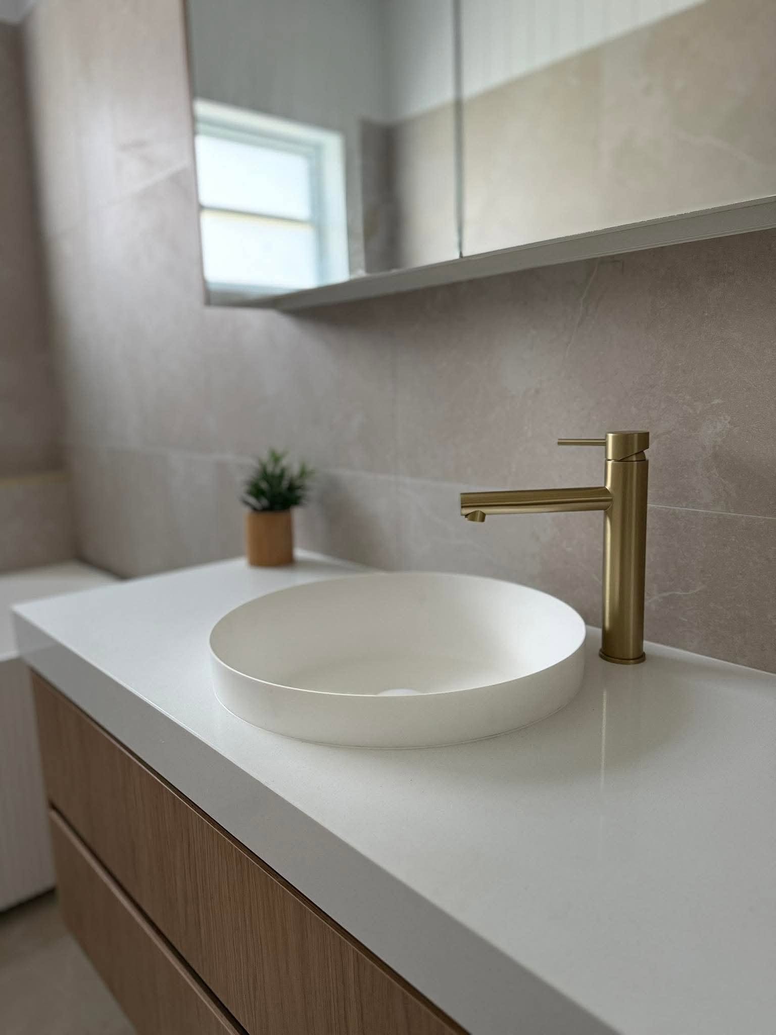 A custom bathroom vanity with a round basin and brushed brass tapware