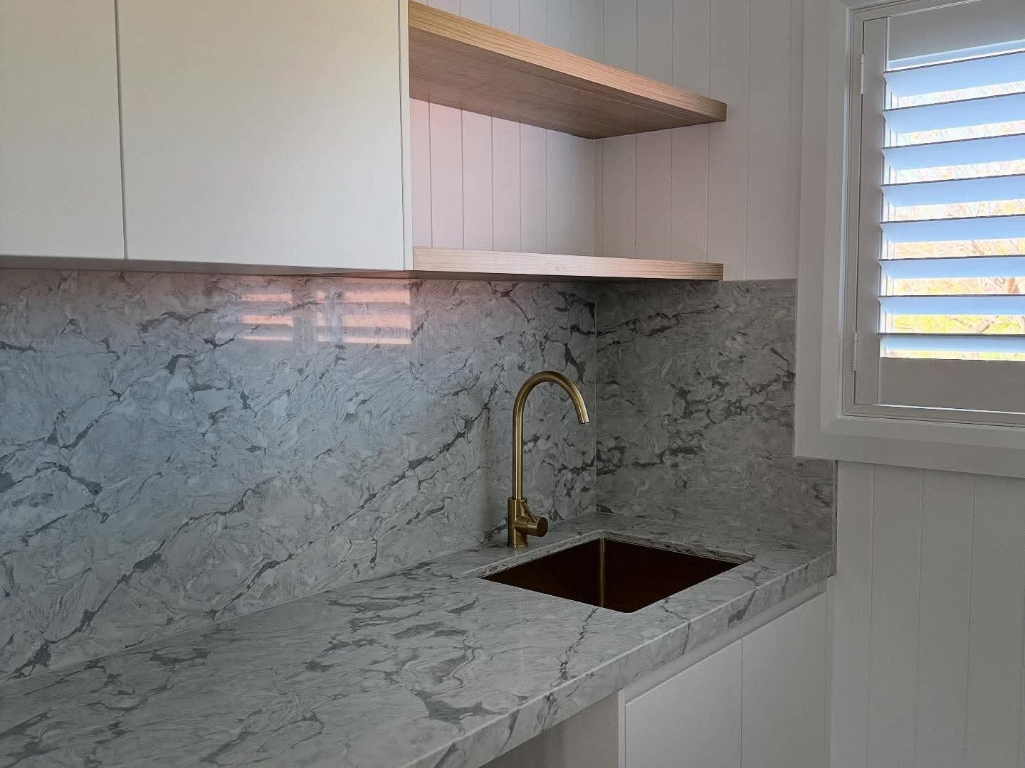 A marble-look stone benchtop with brushed brass tapware by Fabrite Kitchens