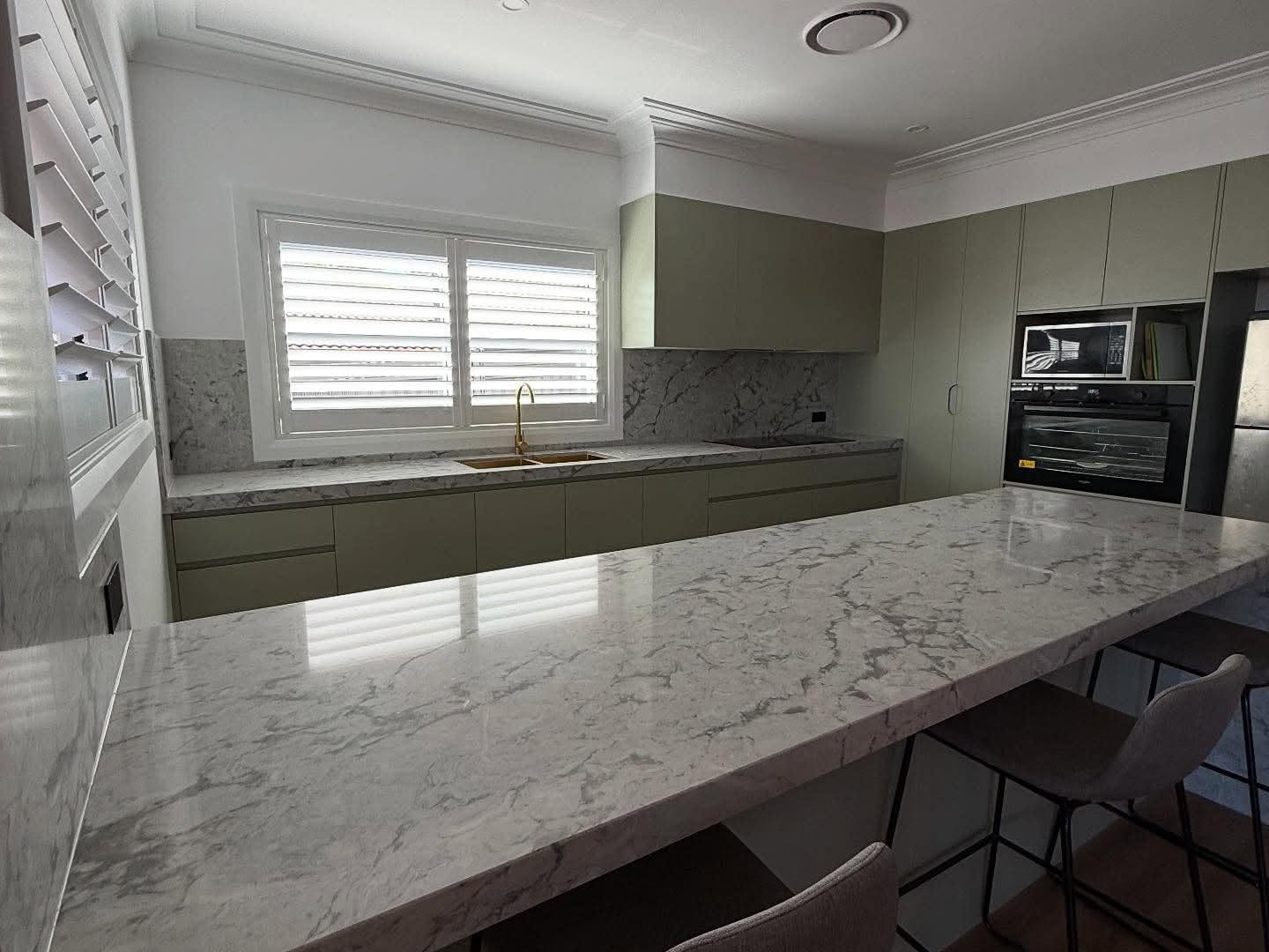 A custom kitchen with a long marble-look stone benchtop, built by Fabrite Kitchens