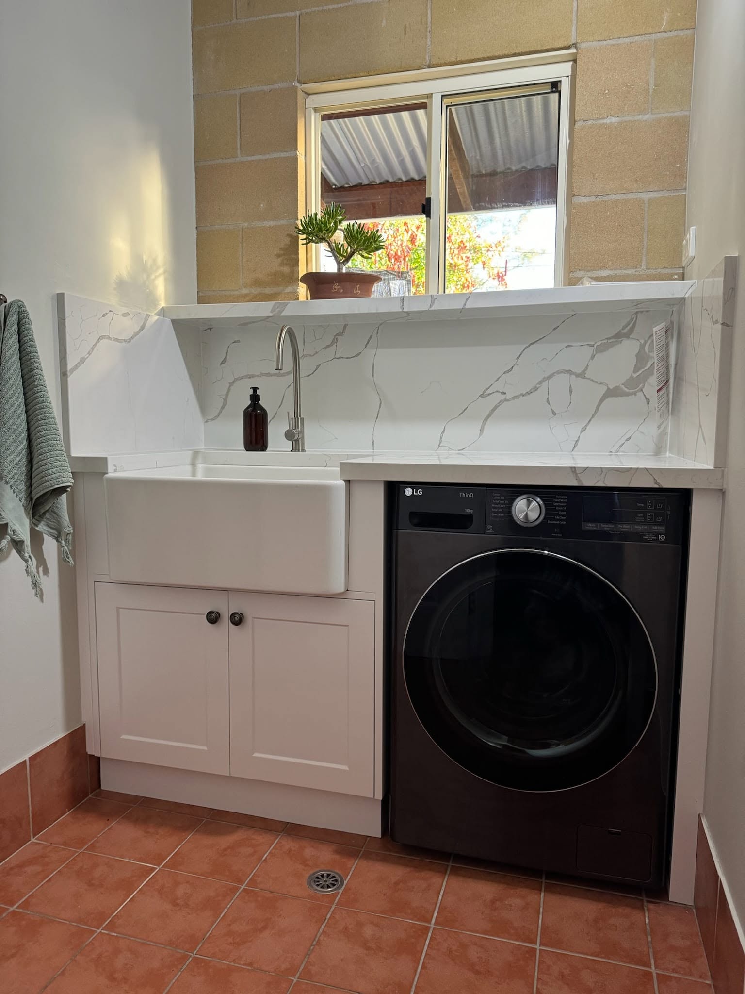 A custom laundry with a farmhouse sink and stone benchtop