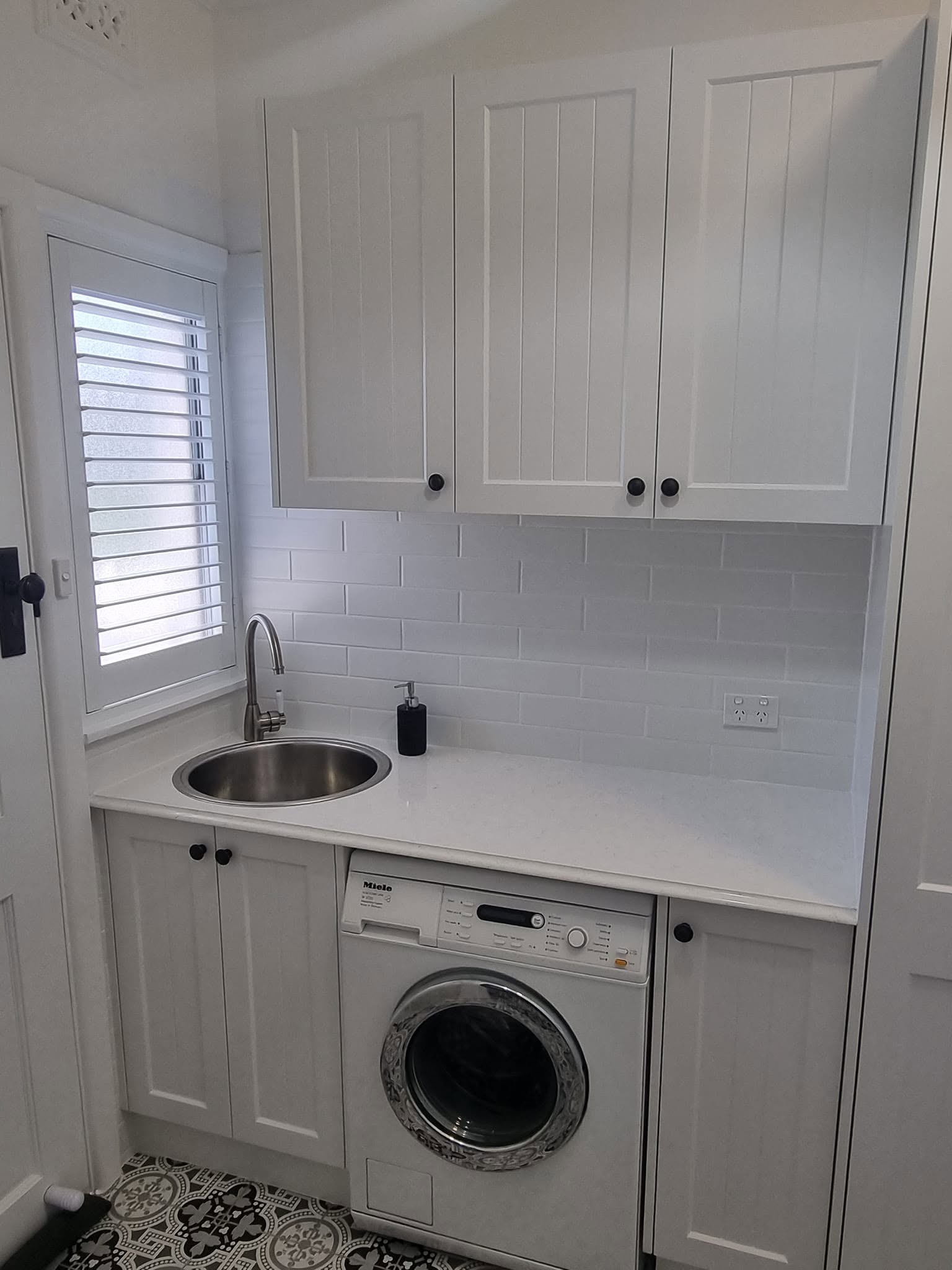 A compact laundry with round sink and under-bench appliances